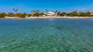 Une propriété située en bord de mer, avec une eau cristalline, des palmiers et un bâtiment blanc.