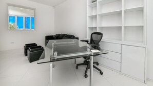 Un ufficio moderno con scrivania in vetro, sedia da ufficio nera e scaffali bianchi.