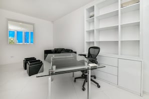 A modern office space with a glass desk, black office chair, and white shelving units. - Oceanfront 8BR Villa w Pool, Patio near Palm Beach (Malmok)
