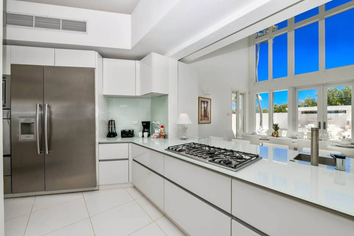 Cocina moderna con refrigerador de acero inoxidable, estufa a gas y un amplio ventanal con vista al cielo azul.