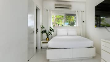 A modern bedroom with a bed, a bedside table, a potted plant, and a window with curtains.