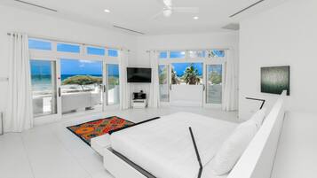 A modern bedroom with a large bed, a flat-screen TV, and a view of the ocean.