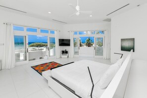A modern bedroom with a large bed, a flat-screen TV, and a view of the ocean.