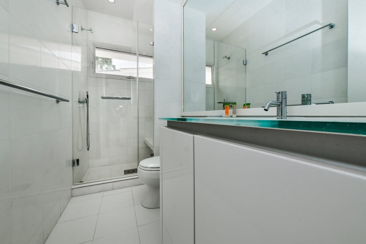 A modern bathroom with a glass shower enclosure, a white toilet, and a large mirror above the sink.