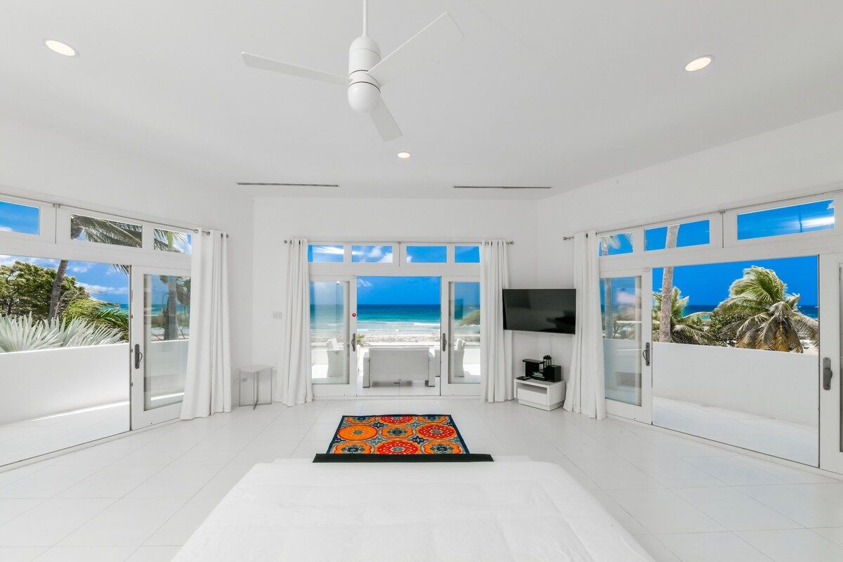 A spacious room with a large sliding glass door leading to a balcony with a view of the beach.