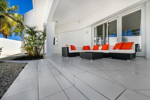 A modern outdoor seating area with a white and black sofa set, red cushions, and a glass door leading to a pool. - Oceanfront 8BR Villa w Pool, Patio near Palm Beach (Malmok)