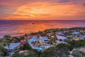 A coastal resort with multiple buildings, a swimming pool, and a view of the ocean at sunset. - Oceanfront 8BR Villa w Pool, Patio near Palm Beach (Malmok)