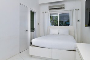 A bedroom with a bed, an air conditioning unit, a window with curtains, and a white door.