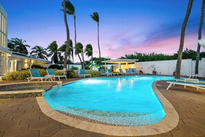 Una piscina con sillas de descanso, palmeras y un edificio al fondo.