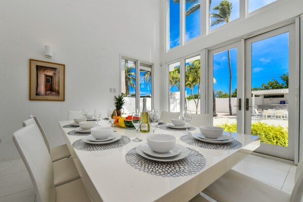 A dining area with a white table set for four, large windows, and a view of palm trees.