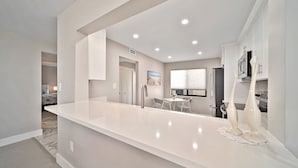 Una cocina moderna con una isla central, armarios blancos y un comedor con mesa y sillas.