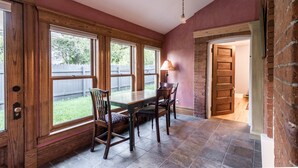 A dining area with a wooden table and chairs, large windows, and a brick wall.