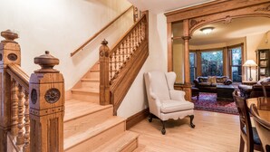 A wooden staircase with a white armchair and a sofa in a well-lit living room with large windows.