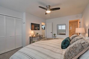 Ein Schlafzimmer mit Bett, Deckenventilator, Schreibtisch mit Lampe, Spiegel und Kleiderschrank.