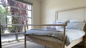 A neatly made bed with a wooden frame, a window with a view of trees, and a carpeted floor.