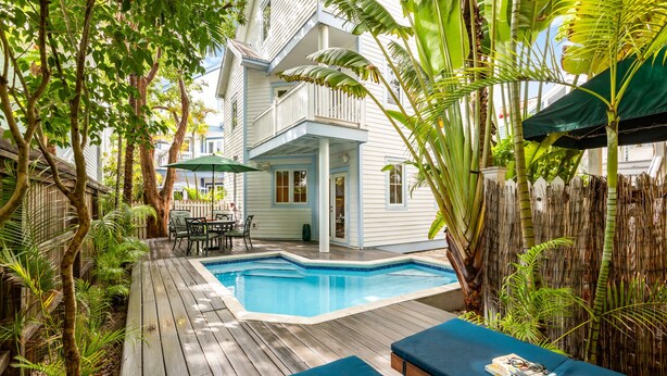 A poolside area with a wooden deck, lounge chairs, and a small table with books. - A KEY ESCAPE ~ 3 Bedroom, 2.5 Bathroom Home in Old Town /Private Heated Pool! (Key West)