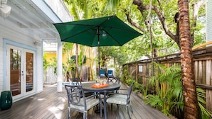 A wooden deck with a table and chairs, surrounded by lush greenery and a wooden fence. - A KEY ESCAPE ~ 3 Bedroom, 2.5 Bathroom Home in Old Town /Private Heated Pool! (Key West)