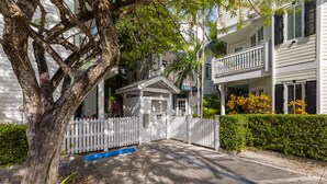 A residential street with a white picket fence, a tree, and a two-story house with a balcony. - A KEY ESCAPE ~ 3 Bedroom, 2.5 Bathroom Home in Old Town /Private Heated Pool! (Key West)