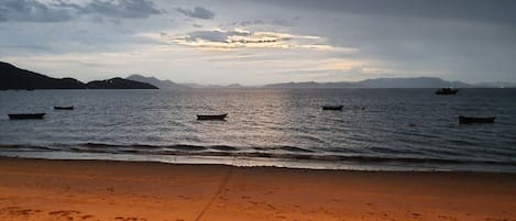 Una playa con barcos sobre aguas tranquilas y montañas a lo lejos.