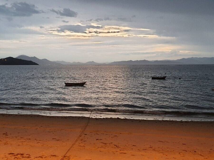 A beach with boats on calm water and distant mountains.