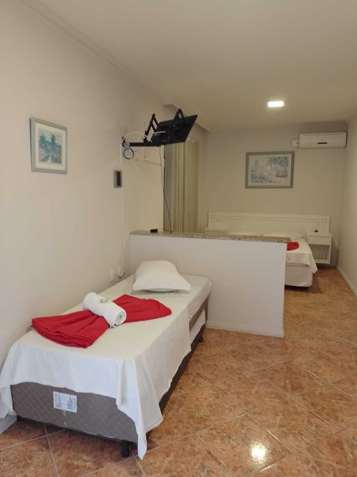 A hotel room with two single beds, a small table, a mirror, and an air conditioning unit on the wall.