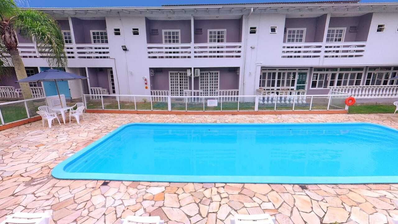 Una piscina con bordo in pietra, sedie bianche e un edificio sullo sfondo con numerosi balconi.