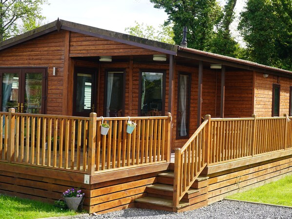 A wooden cabin with a covered porch and a small set of steps leading to the entrance. - Roe Deer Lodge (Newton Stewart)
