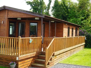A wooden cabin with a porch, steps, and a small garden area. - Roe Deer Lodge (Newton Stewart)