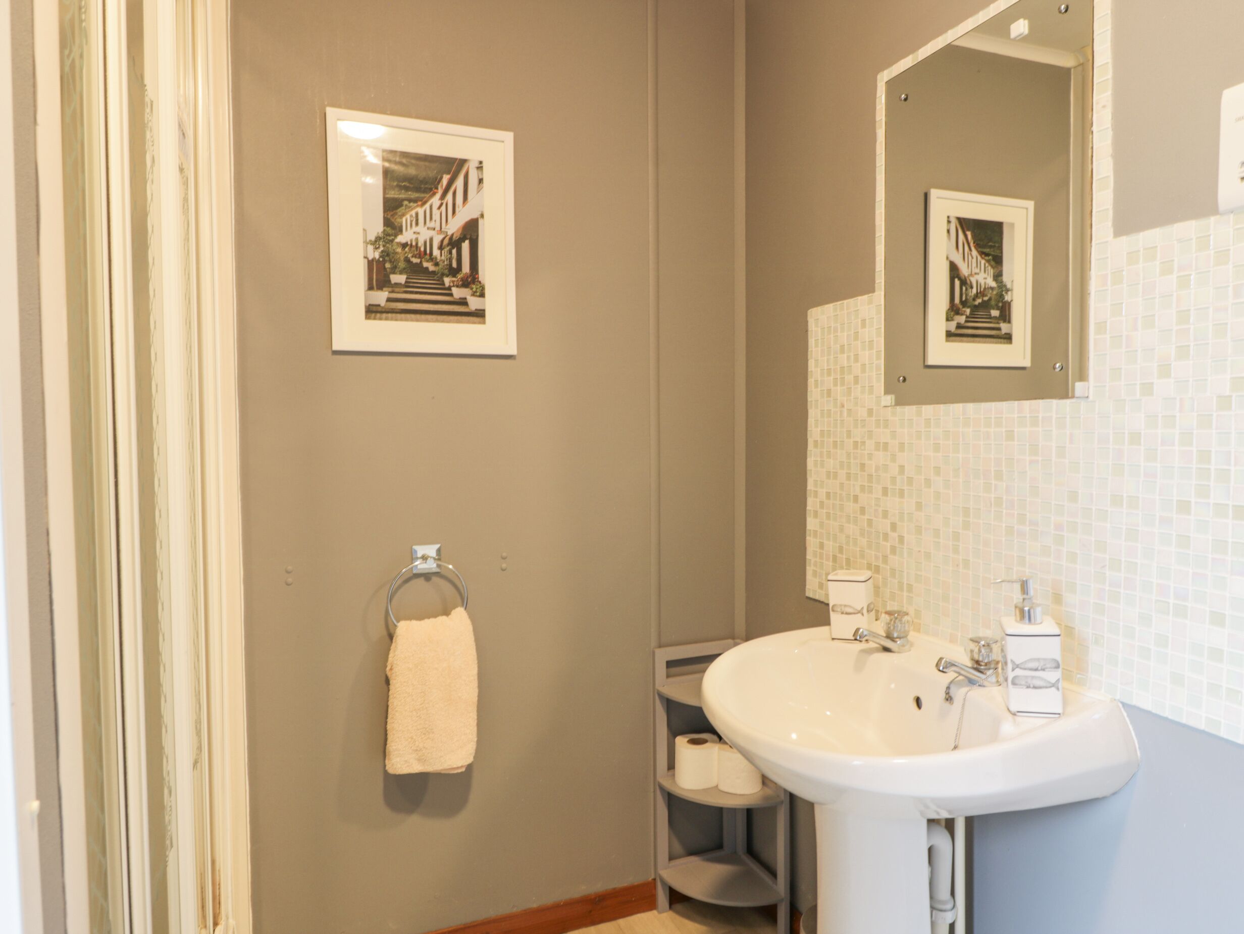 Une salle de bain équipée d’un lavabo, d’un miroir, d’un porte-serviettes et de deux tableaux encadrés accrochés au mur.