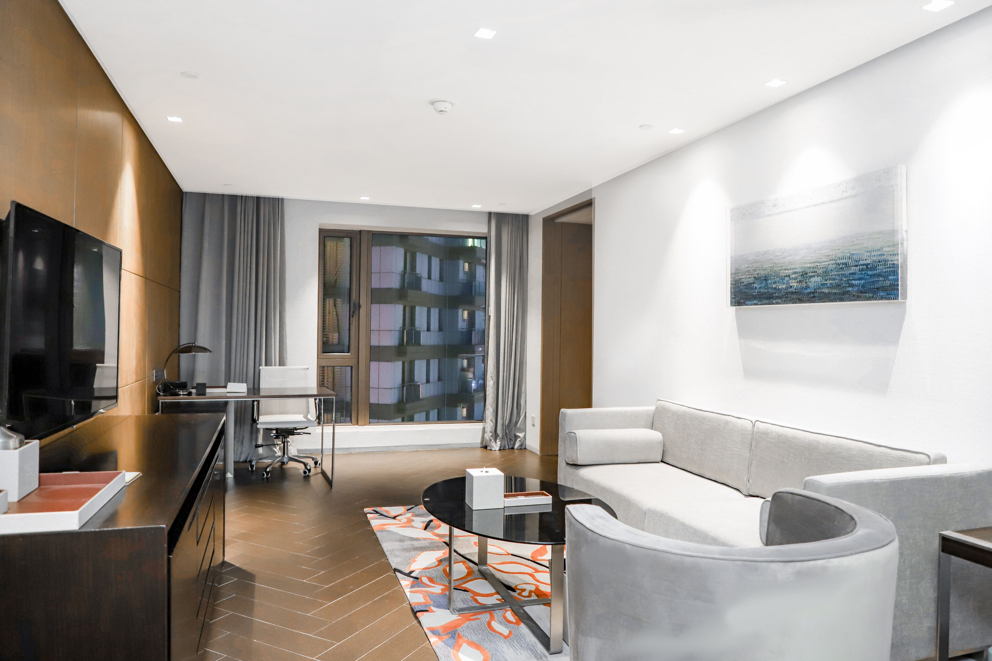 Une chambre d’hôtel moderne équipée d’une télévision à écran plat, d’un canapé, d’une table basse et d’une grande fenêtre donnant sur la ville.