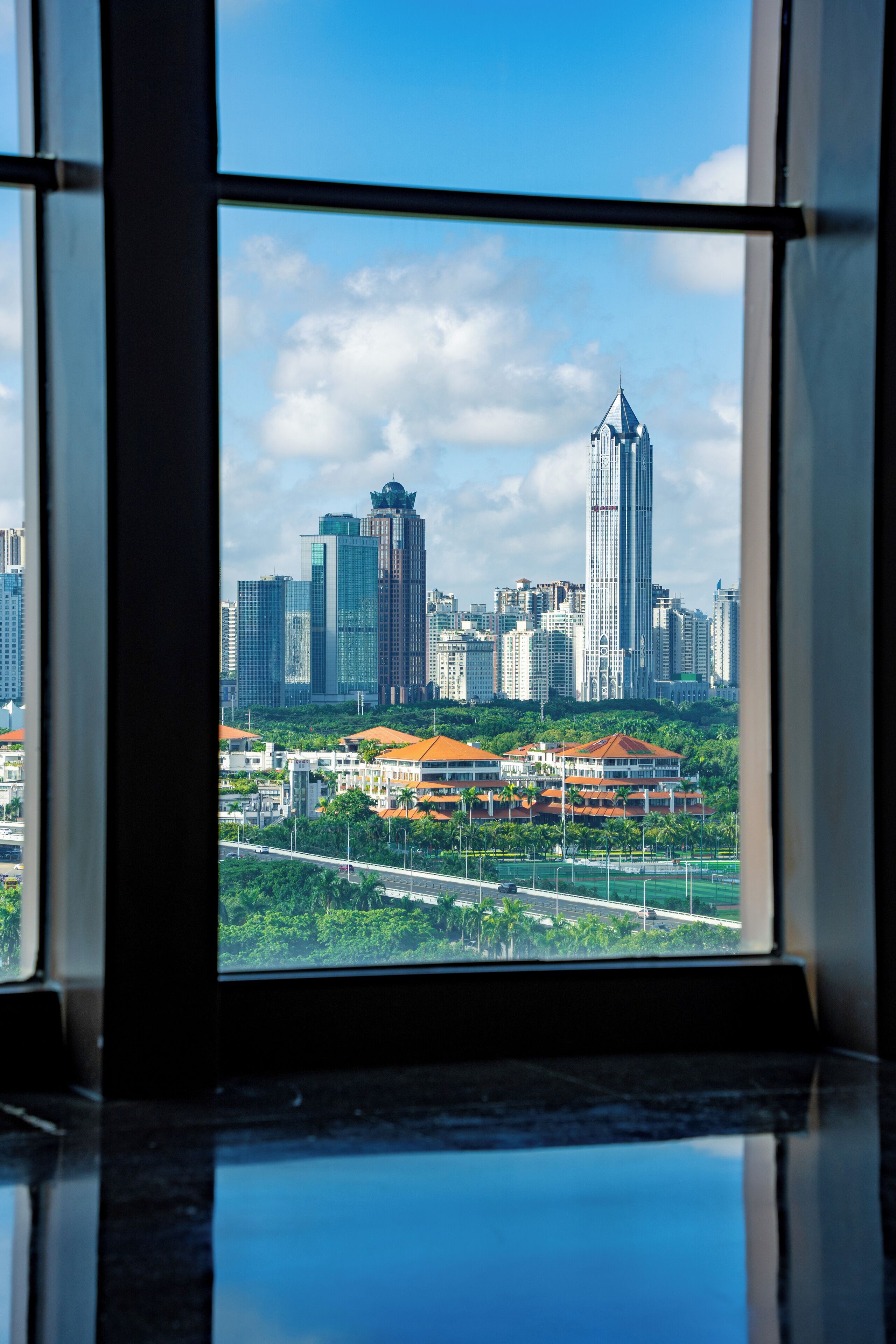 A view from a window of a cityscape with tall buildings, a bridge, and greenery.