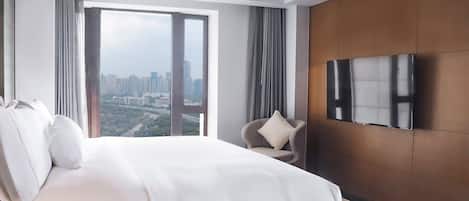 A modern hotel room with a large bed, a TV mounted on the wall, and a view of the cityscape through the window.
