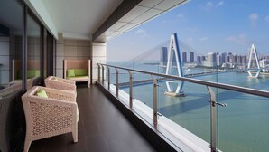 A balcony with wicker furniture and a view of a modern bridge and city skyline. - The Westin Haikou (Haikou)