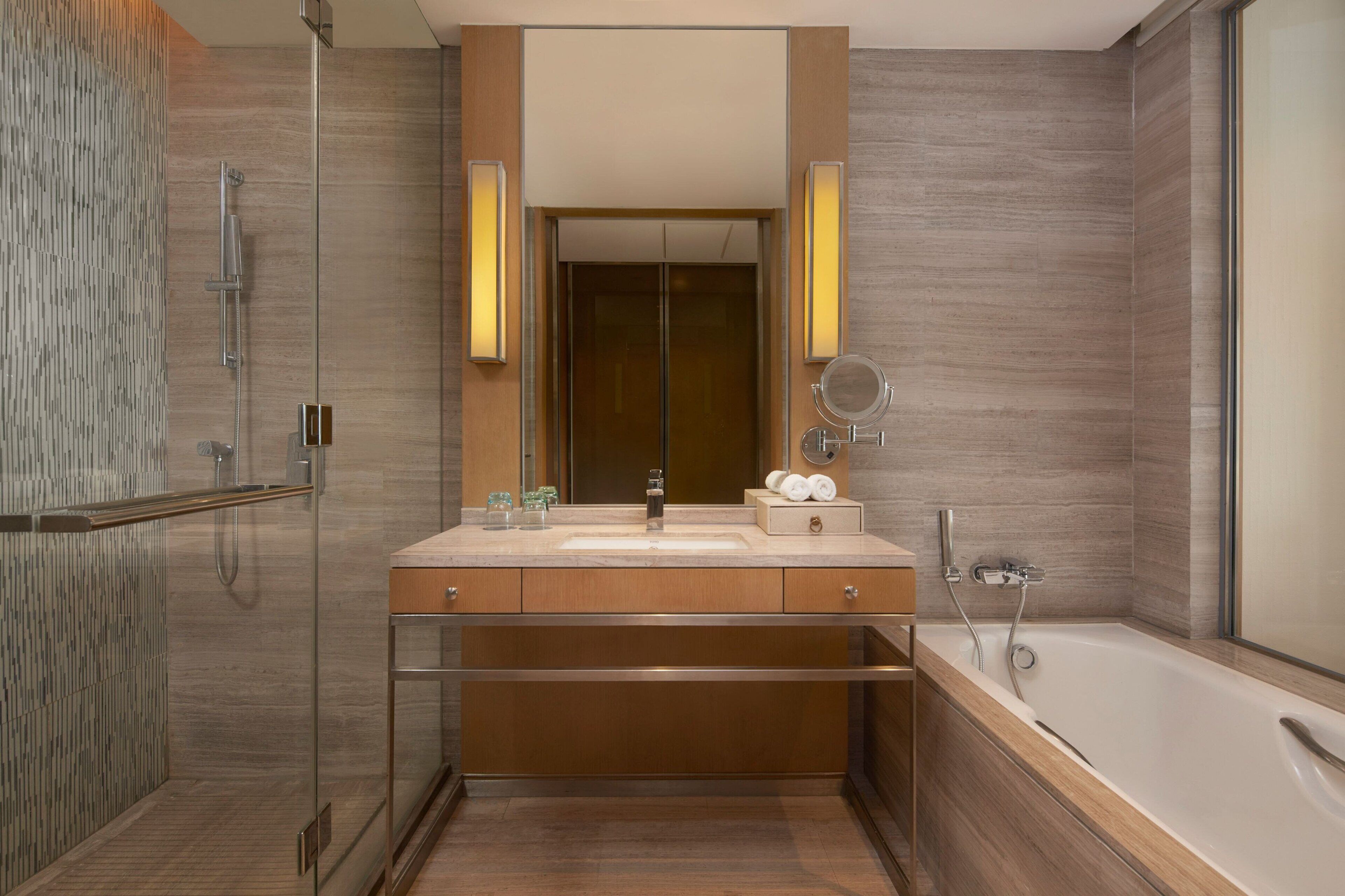 A modern bathroom with a glass shower enclosure, a large mirror, a bathtub, and wooden cabinetry.