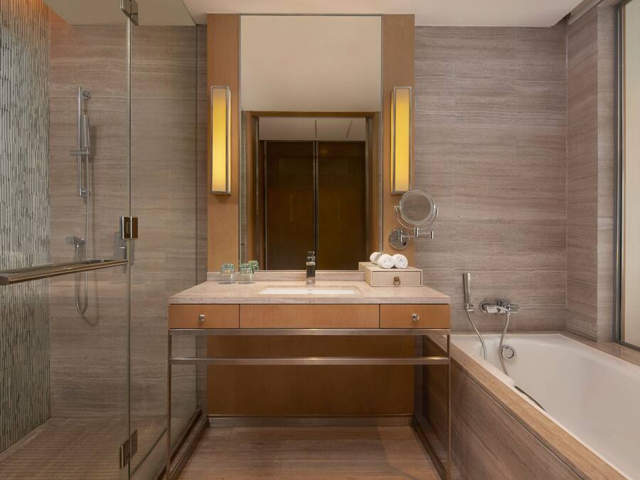 A modern bathroom with a glass shower enclosure, a large mirror, a bathtub, and wooden cabinetry.