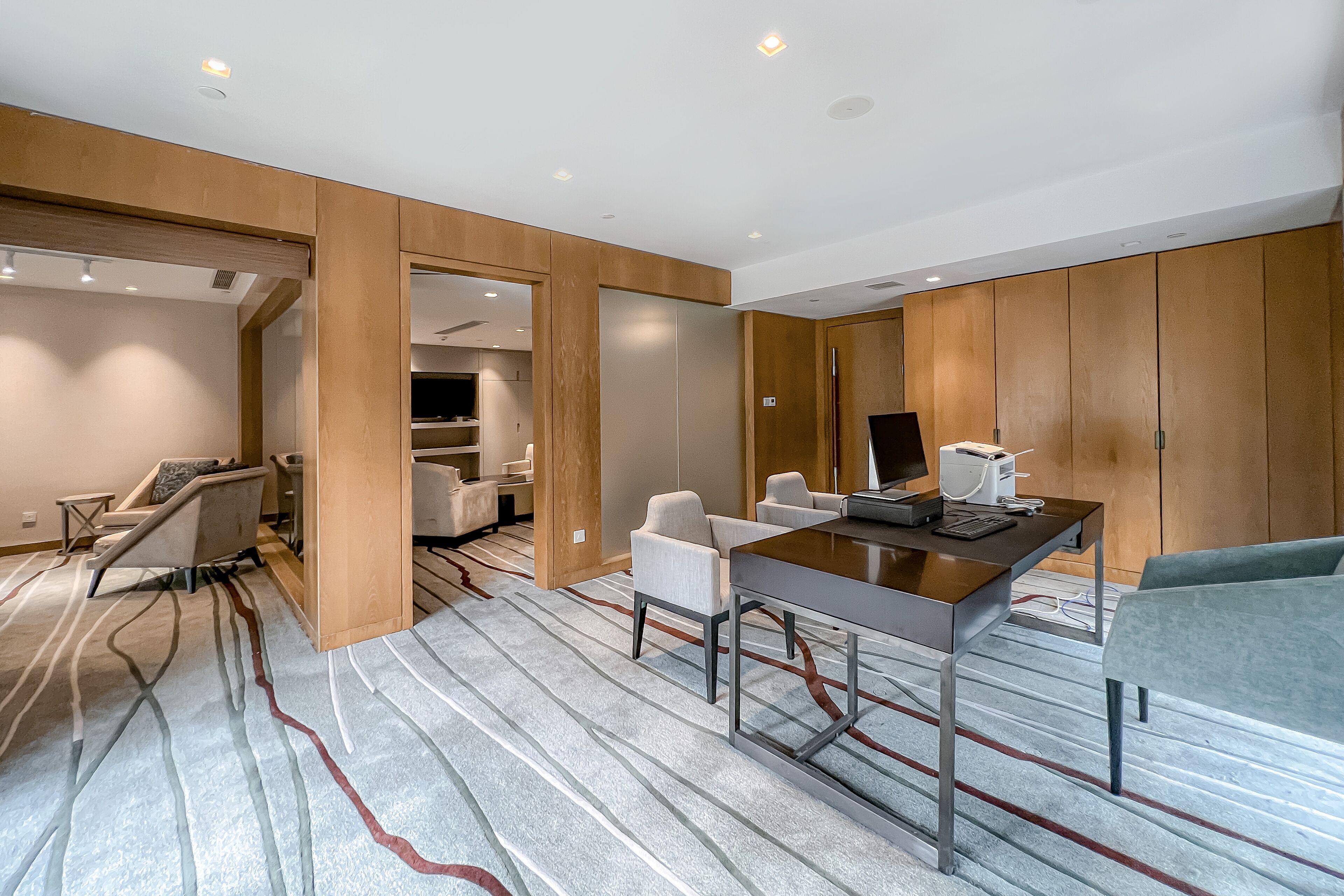 Una habitación de hotel moderna con un panel de pared de madera, una alfombra a rayas, un escritorio con sillas y una cama.