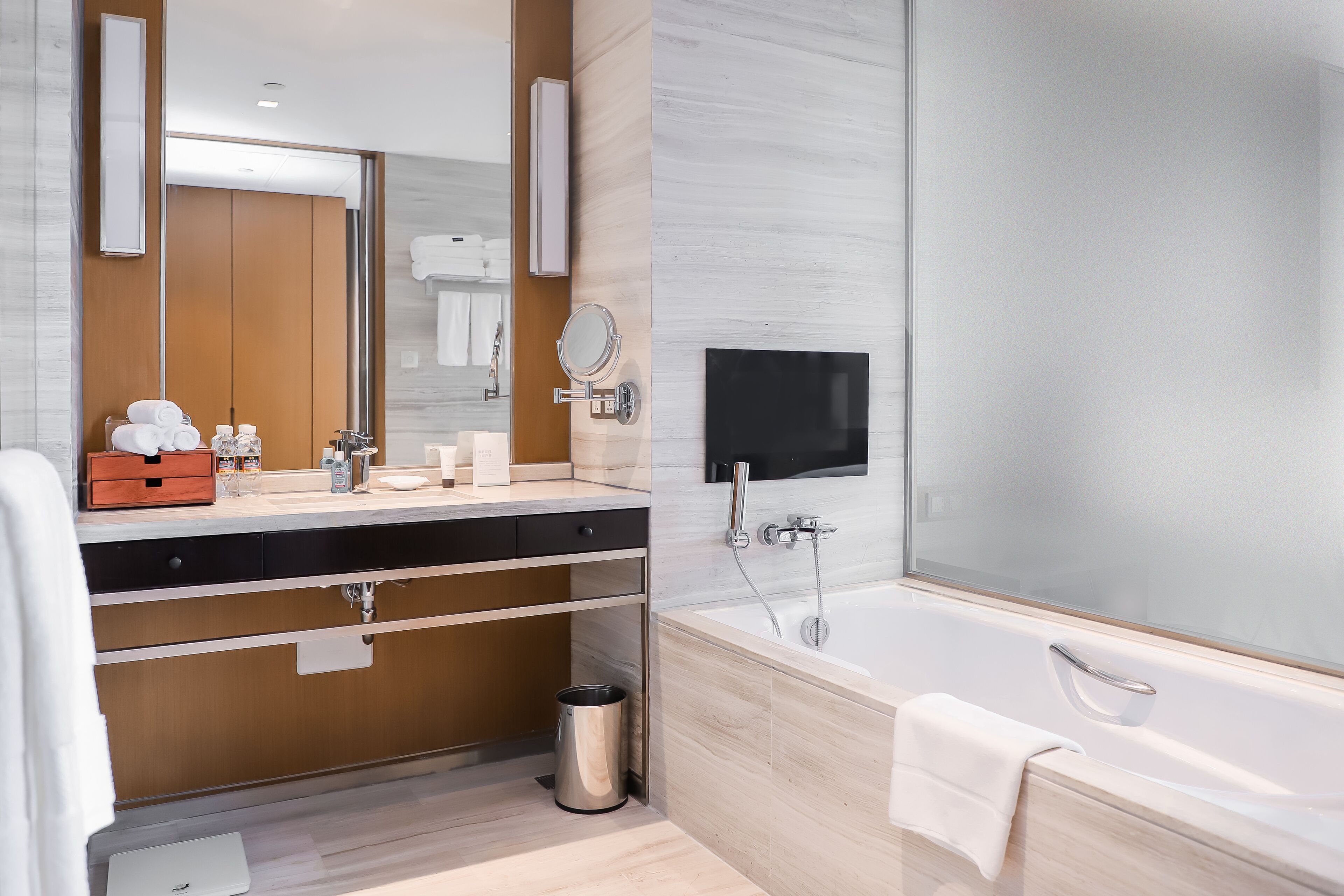 Une salle de bain moderne avec un grand miroir, un meuble-lavabo avec des articles de toilette, une baignoire et une poubelle.