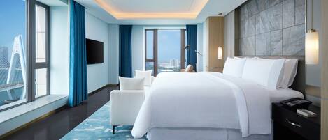 A modern hotel room with a large bed, a sofa, a desk, and a view of the city.