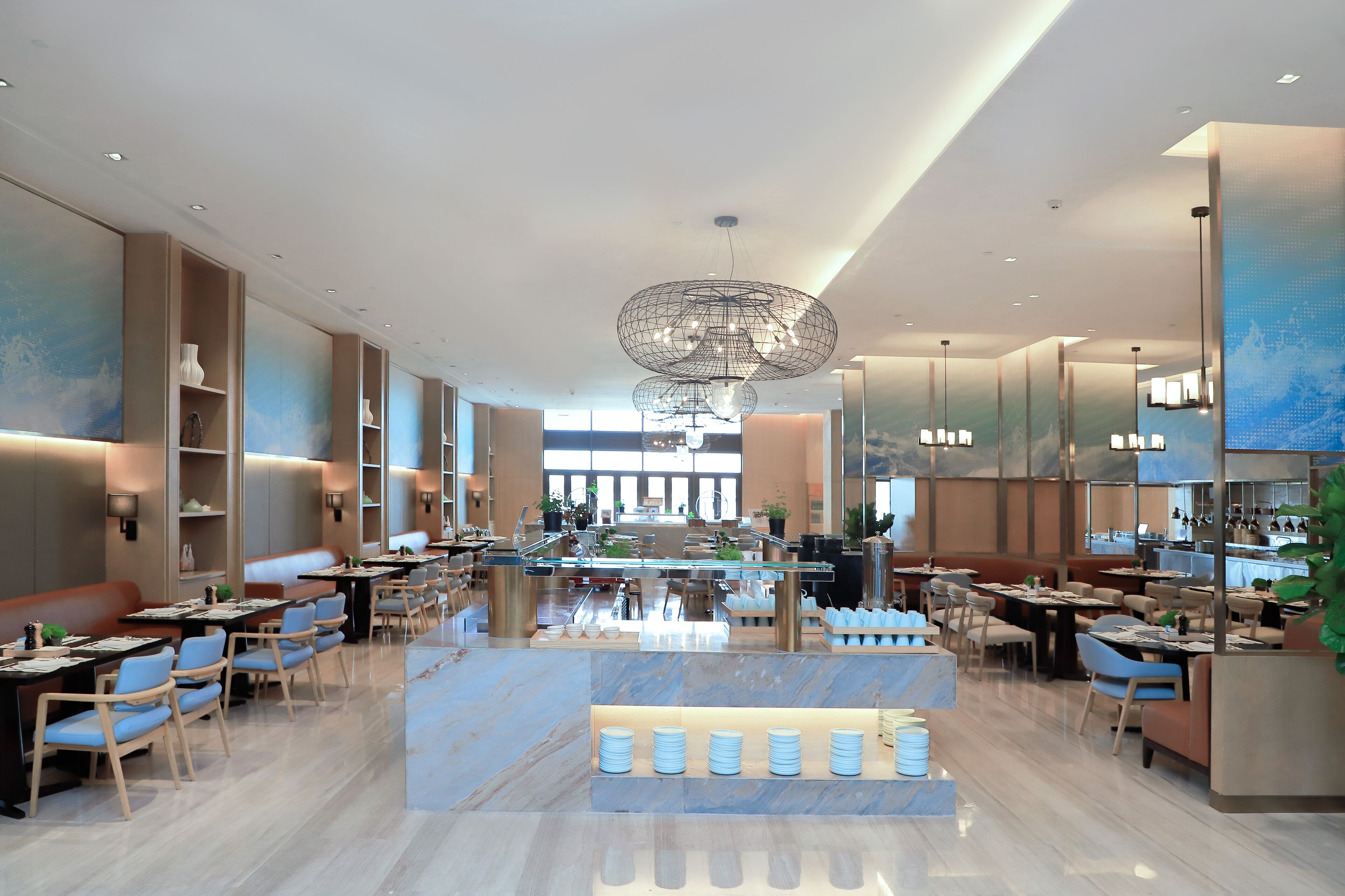 A modern restaurant with a central bar area, multiple seating options, and a contemporary chandelier.