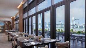 A modern dining area with tables and chairs, large windows with a view of a bridge and cityscape. - The Westin Haikou (Haikou)