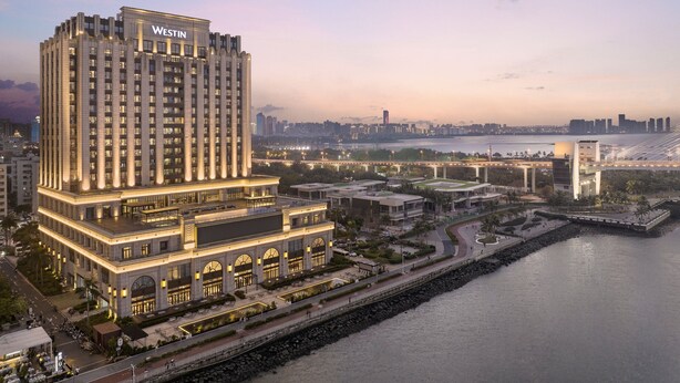 A high-rise hotel with a prominent 'Westin' sign, situated by a waterfront with a bridge and cityscape in the background. - The Westin Haikou (Haikou)