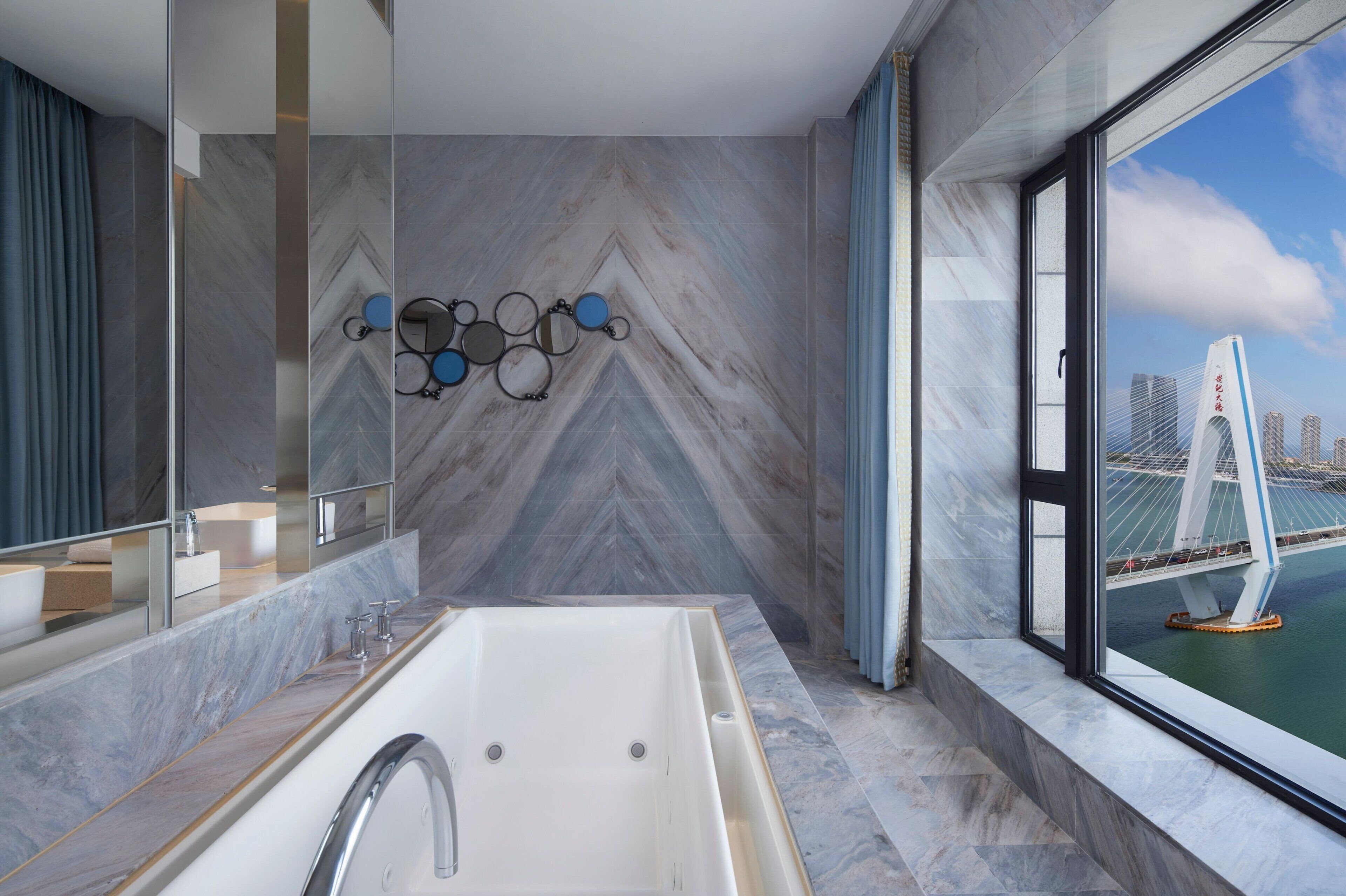 A modern bathroom with a large bathtub, a mirror, and a view of a bridge.