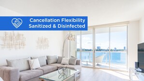 A modern living room with a sofa, a glass coffee table, and a view of a body of water through large windows. - Chic Waterfront Retreat | Panoramic Intracoastal Views (Sunny Isles Beach)