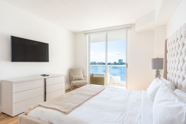 Habitación de hotel moderna con cama, televisión, silla, escritorio y vista al agua.