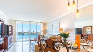 A spacious living area with a large glass door leading to a balcony overlooking a body of water. - Bright & Spacious Condo with Breathtaking Bay Views + WiFi (Sunny Isles Beach)