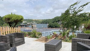 A terrace with wicker furniture, a view of a body of water, and surrounding greenery.