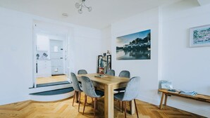 A modern dining area with a wooden table and grey chairs, a bookshelf with books, and a painting of a coastal scene.
