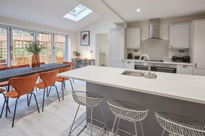 Une cuisine moderne dotée d’un îlot central, de tabourets de bar et d’un coin repas avec des chaises orange.