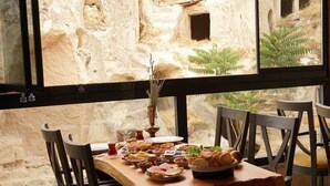 A dining area with a table set for a meal, chairs, and a view of a rocky outdoor area through large windows. - Pome Granate Cave Hotel (Nevsehir)