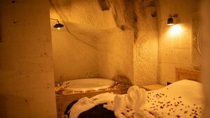 A dimly lit room with a bed, a small table with a glass, and a wall-mounted light fixture. - Pome Granate Cave Hotel (Nevsehir)
